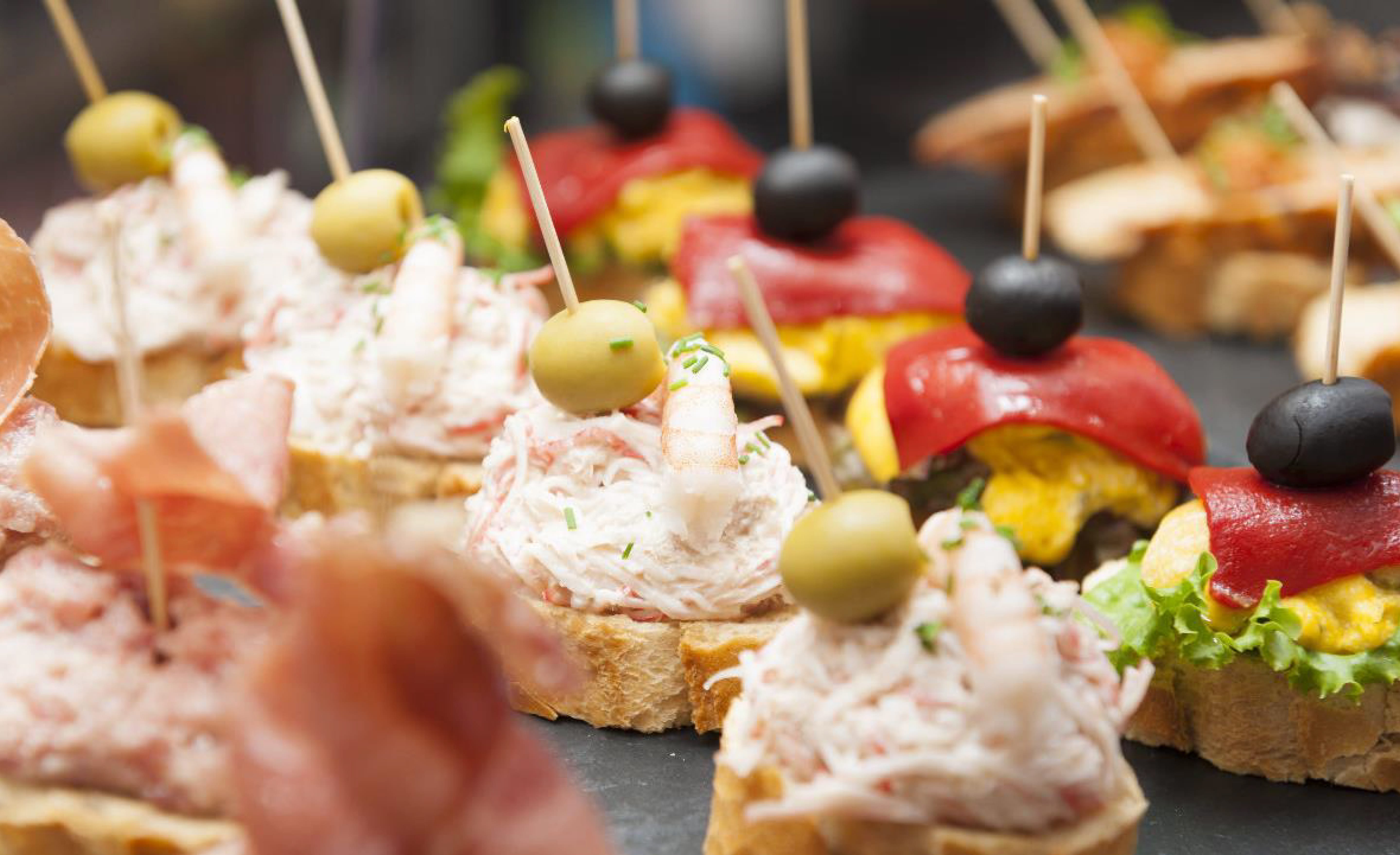 画像：バゲットのスライスの上にオリーブやエビなどが乗せられたスペイン料理のピンチョス